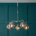 A 5-light polished chrome ceiling pendant with dimpled smoked glass globes against a teal paneled wall.