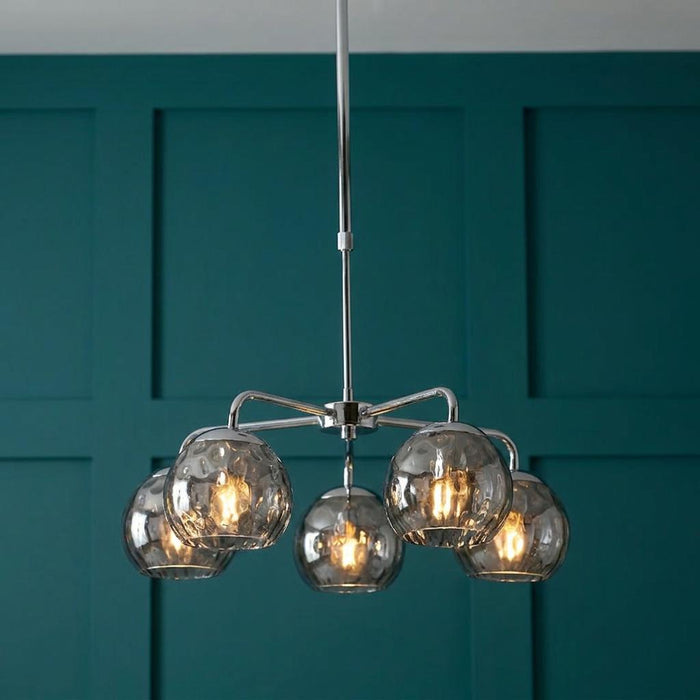 A 5-light polished chrome ceiling pendant with dimpled smoked glass globes against a teal paneled wall.