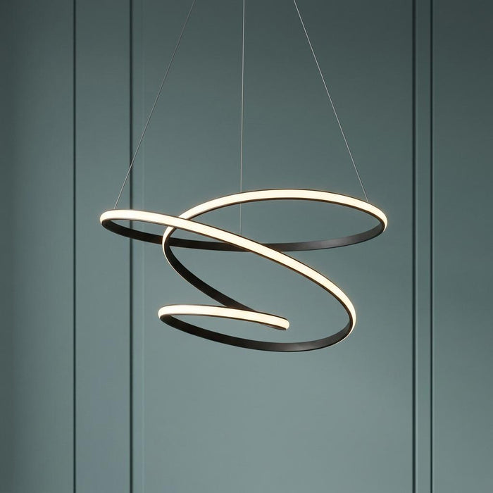 Swirling black LED pendant light with a ribbon design, suspended against a muted green paneled wall.