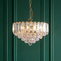 Brass and acrylic crystal chandelier pendant illuminated against a dark green paneled wall.