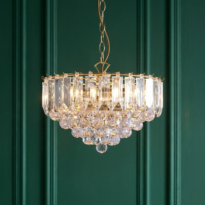 Brass and acrylic crystal chandelier pendant illuminated against a dark green paneled wall.