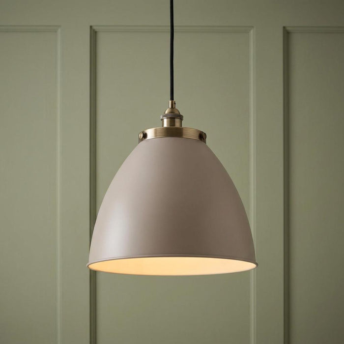 Stone colored dome pendant light with brass hardware hanging in front of a green paneled wall.