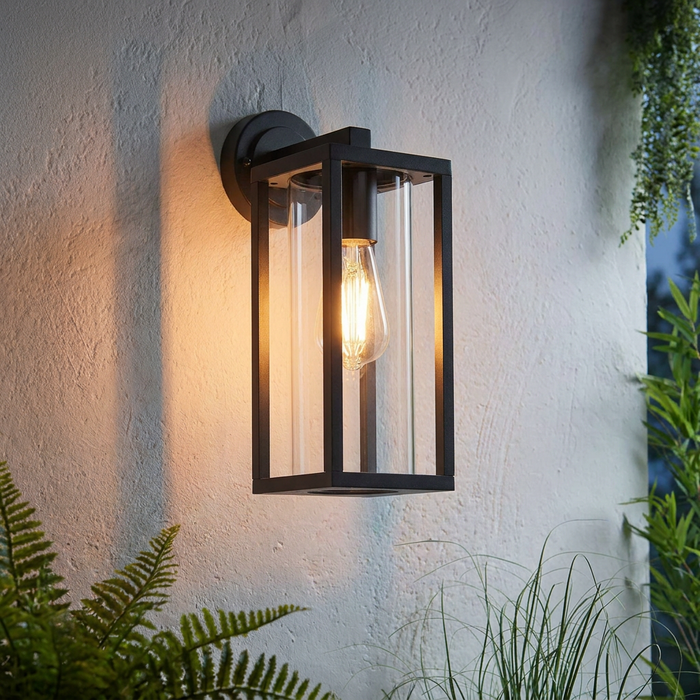 Endon Hamden black outdoor wall light with a glowing filament bulb and glass cylinder, mounted on a white textured wall.