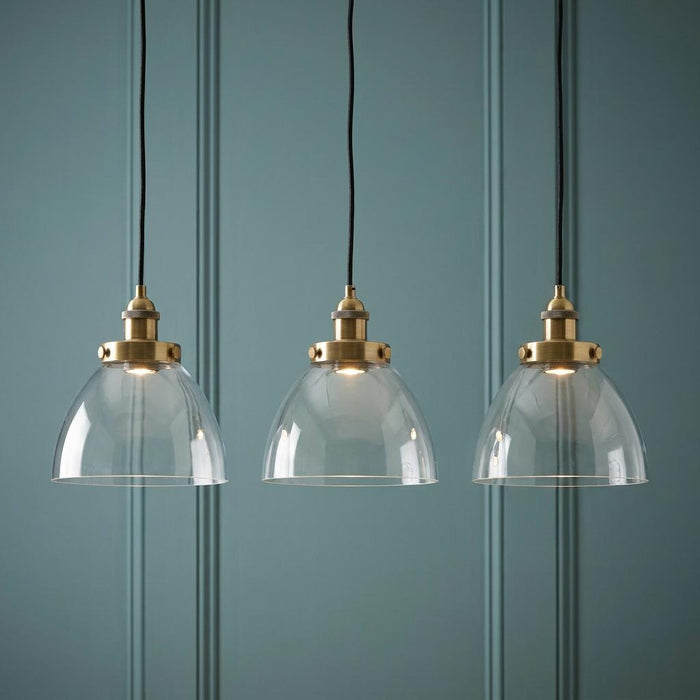 Three brass pendant lights with glass dome shades suspended against a teal wood-paneled wall.