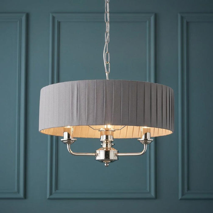 3-light pendant featuring a charcoal pleated shade and bright nickel finish set against a teal paneled wall.