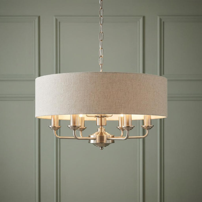 Endon Highclere 6-light pendant in brushed chrome with a natural linen drum shade against a green paneled wall.
