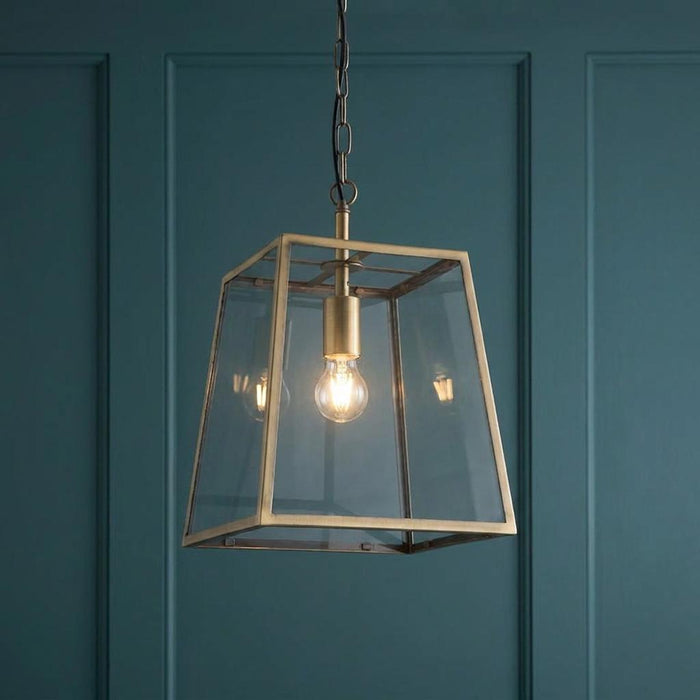 Antique brass lantern pendant light with glass panels hanging against a dark teal paneled wall.