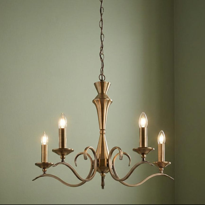 Endon Kora antique brass 5-light chandelier with curved arms and glowing candle bulbs against a sage wall.