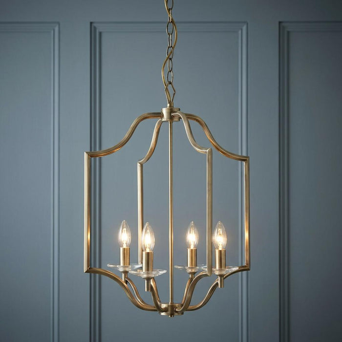Four-light antique brass lantern pendant with candle bulbs hanging against a blue paneled wall.