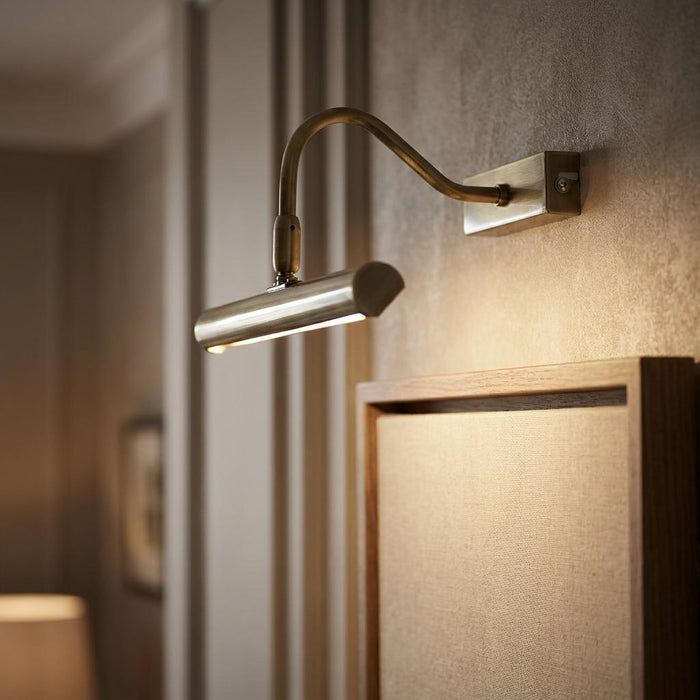 Antique brass LED picture light mounted on a wall and illuminating a framed canvas.