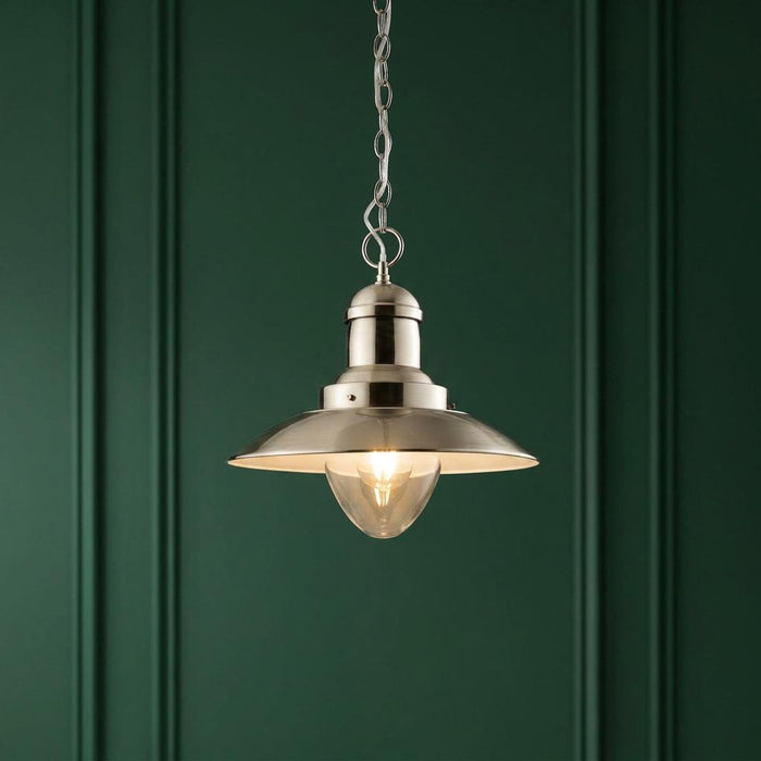 Polished nickel ceiling pendant light with a glass shade hanging against a deep green paneled wall.