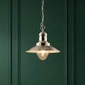 Polished nickel ceiling pendant light with a glass shade hanging against a deep green paneled wall.
