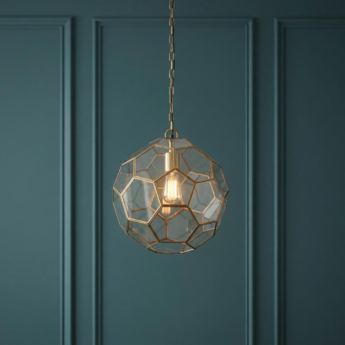 A geometric brass and glass globe pendant light with an Edison bulb hanging against a teal paneled wall.