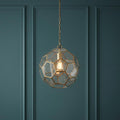 A geometric brass and glass globe pendant light with an Edison bulb hanging against a teal paneled wall.