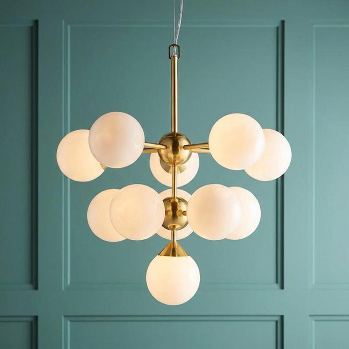 Modern brass pendant light with eleven white globe shades against a teal paneled background.