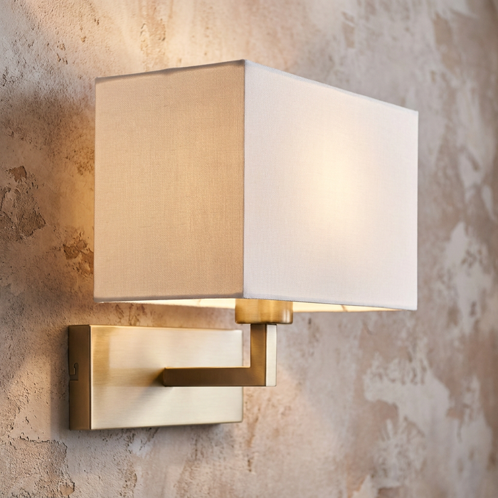 Modern brass wall light with a white rectangular fabric shade mounted on a textured wall.