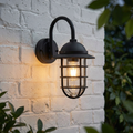 Black caged outdoor wall light with a glowing filament bulb mounted on a white brick wall.
