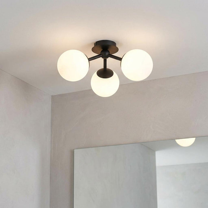 Semi-flush black bathroom ceiling light with three glowing opal glass globe shades mounted on a plain ceiling.