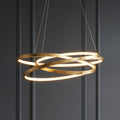 Modern gold leaf LED pendant light with intertwined rings glowing against a dark grey paneled wall.