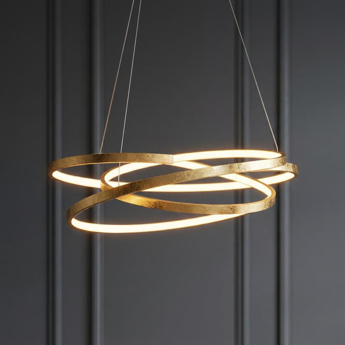 Modern gold leaf LED pendant light with intertwined rings glowing against a dark grey paneled wall.