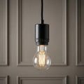Minimalist black pendant light fixing with a clear filament bulb glowing against a paneled wall.