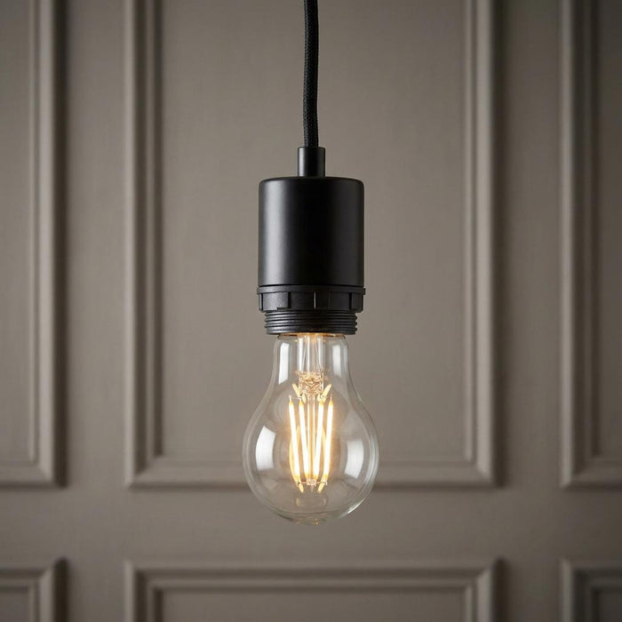 Minimalist black pendant light fixing with a clear filament bulb glowing against a paneled wall.