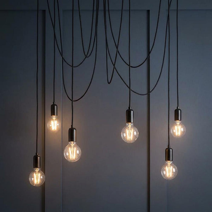 Industrial black six-light pendant fixture with exposed filament bulbs hanging at varying levels against a dark wall.