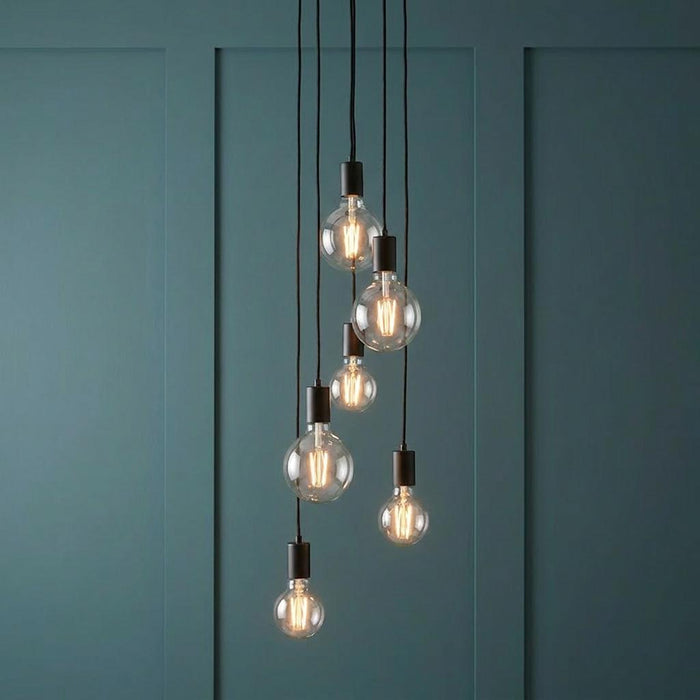 Six black pendant lights with clear globe bulbs hang at staggered heights against a teal paneled wall.