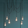Endon Studio 6 light copper ceiling pendant with exposed Edison bulbs against a teal panelled wall.