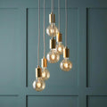 Six gold-capped pendant lights with glowing globe bulbs hanging at tiered heights against a teal paneled wall.
