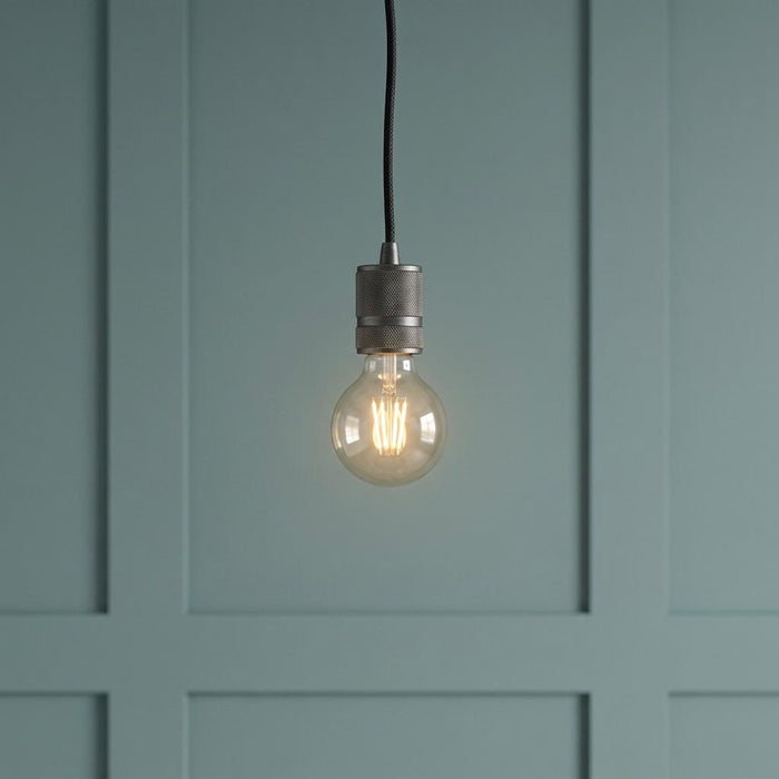 Industrial pendant light with a textured metal socket and glowing filament bulb against a teal paneled wall.