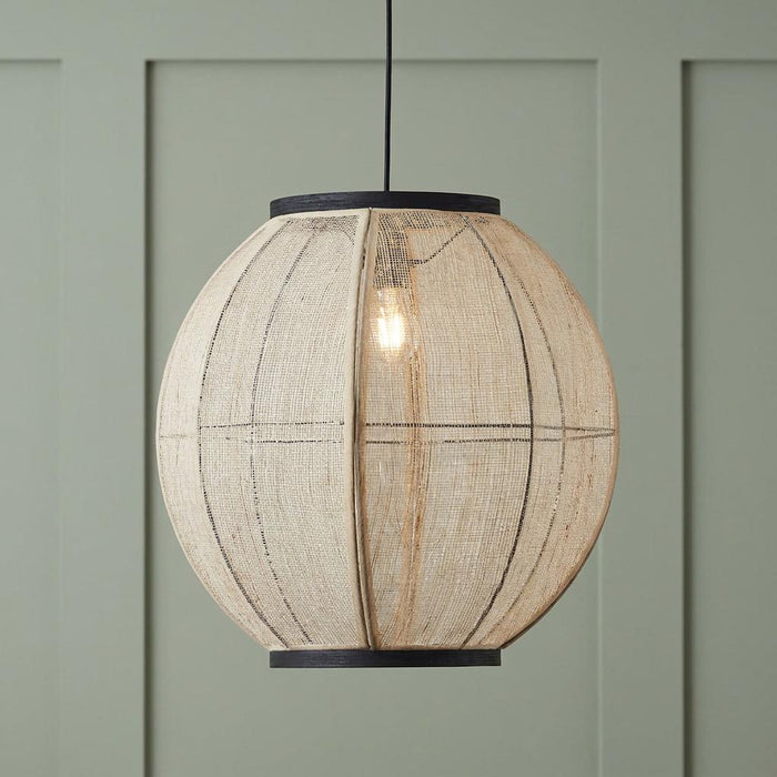 Natural linen globe pendant light with black trim, illuminated in front of a sage green paneled wall.