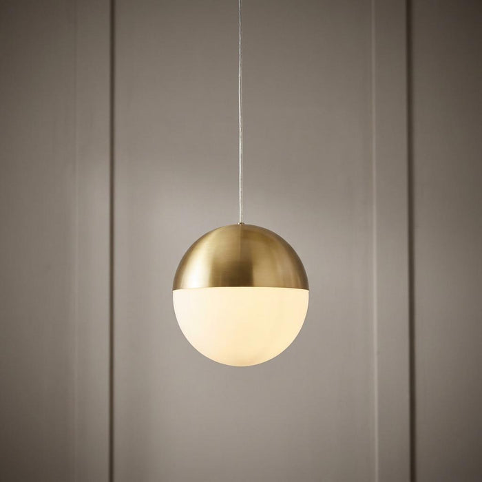 Spherical pendant light with a brushed brass top and opal glass shade, hanging against a grey panelled wall.