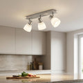 Three-light nickel bar spotlight with satin glass shades mounted on a kitchen ceiling, illuminating an island.