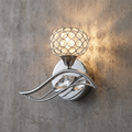 Chrome wall light with crystal globe shade and decorative curved arm mounted on a concrete wall.