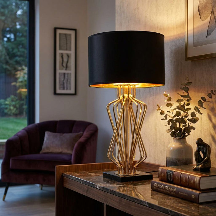 Gold sculptural wire table lamp with a black drum shade on a marble-top console in a modern living room.