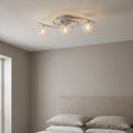 3-light polished chrome semi-flush ceiling light with crystal globes mounted above a bed in a modern bedroom.