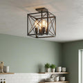 Square cage lantern ceiling light with four glowing filament bulbs installed in a kitchen with green walls.
