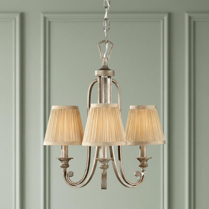 Feiss Abbey 3-light chandelier with silver leaf finish and pleated fabric shades against a green paneled wall.
