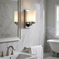 Feiss Amalia polished chrome wall sconce with a cylindrical shade on a marble bathroom wall next to a mirror.