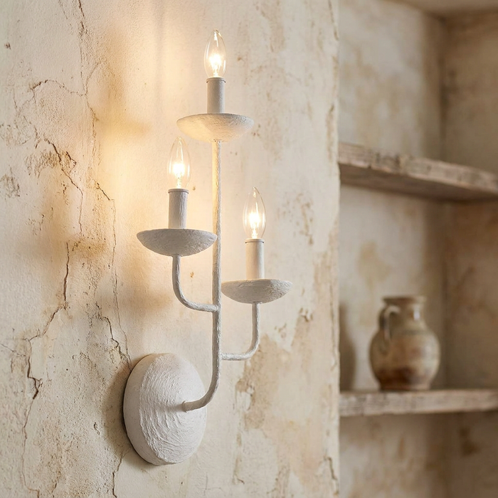 Feiss Annie three-light white wall sconce with a plaster-like texture mounted on a rustic aged wall.