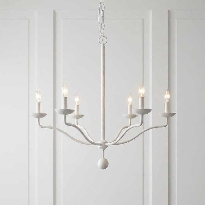 Feiss Annie six-light textured white chandelier with lit candle bulbs against a white paneled wall.