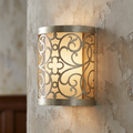 Feiss Arabesque silver leaf wall sconce with a laser-cut scrollwork frame over an ivory linen shade on a textured wall.