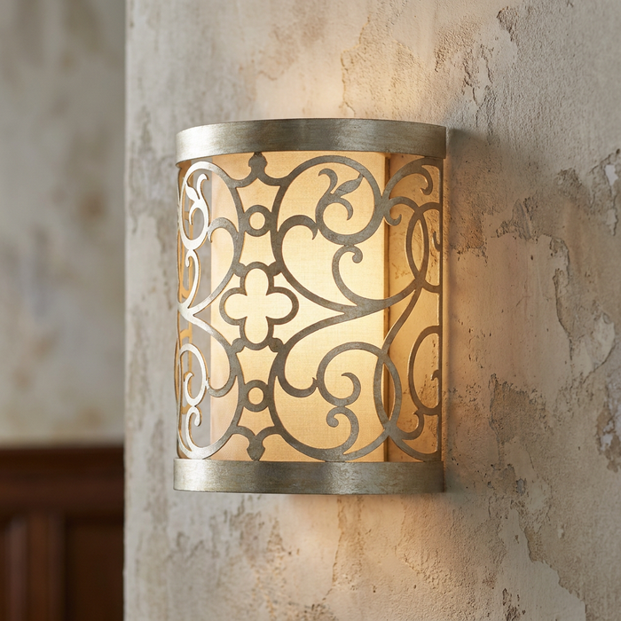 Feiss Arabesque silver leaf wall sconce with a laser-cut scrollwork frame over an ivory linen shade on a textured wall.