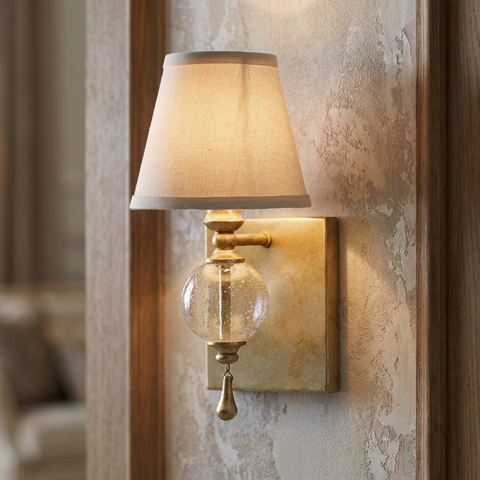 Feiss Argento wall light with fabric shade, seeded glass globe, and gold leaf finish on a textured wall.
