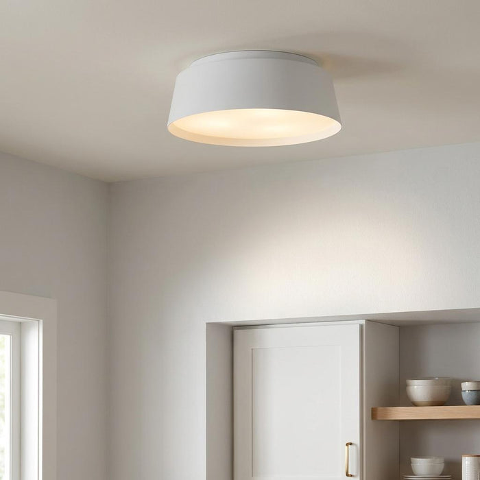 Matte white tapered drum flush mount ceiling light glowing softly in a minimalist white interior.