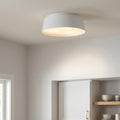 Matte white tapered drum flush mount ceiling light glowing softly in a minimalist white interior.