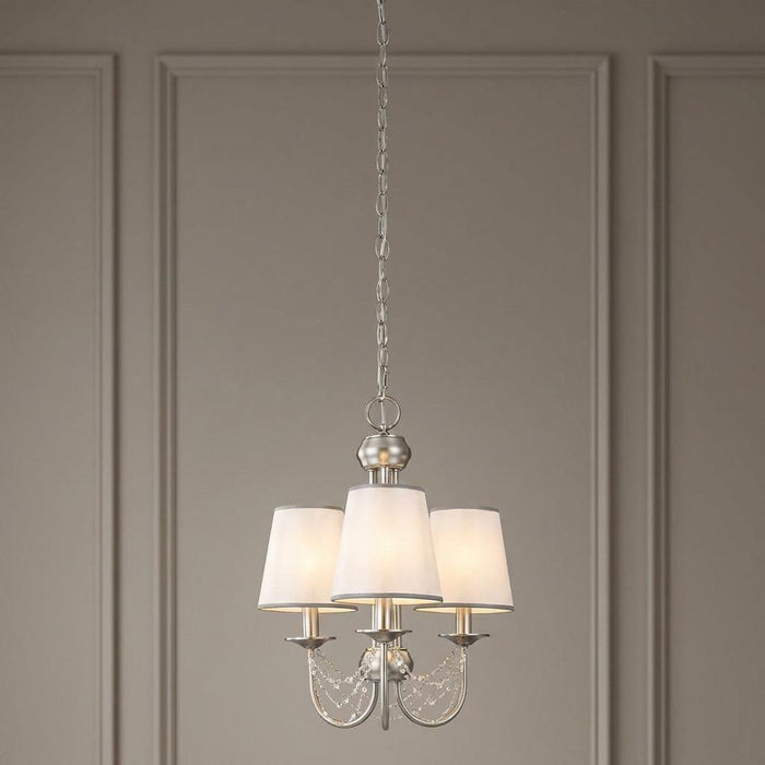 Feiss Aveline three-light brushed steel chandelier with white shades and crystal accents against a paneled wall.