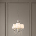 Feiss Aveline three-light brushed steel chandelier with white shades and crystal accents against a paneled wall.