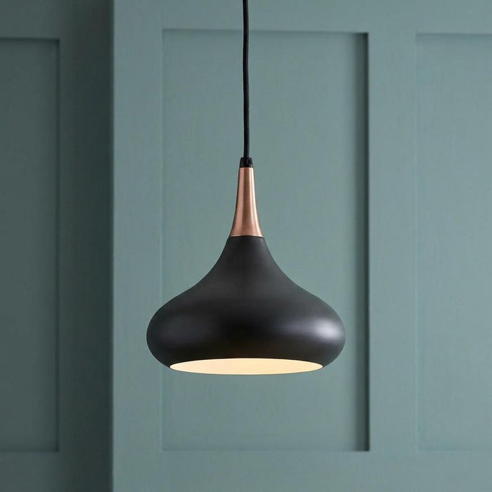 Matte black and copper teardrop pendant light hanging against a green paneled wall.